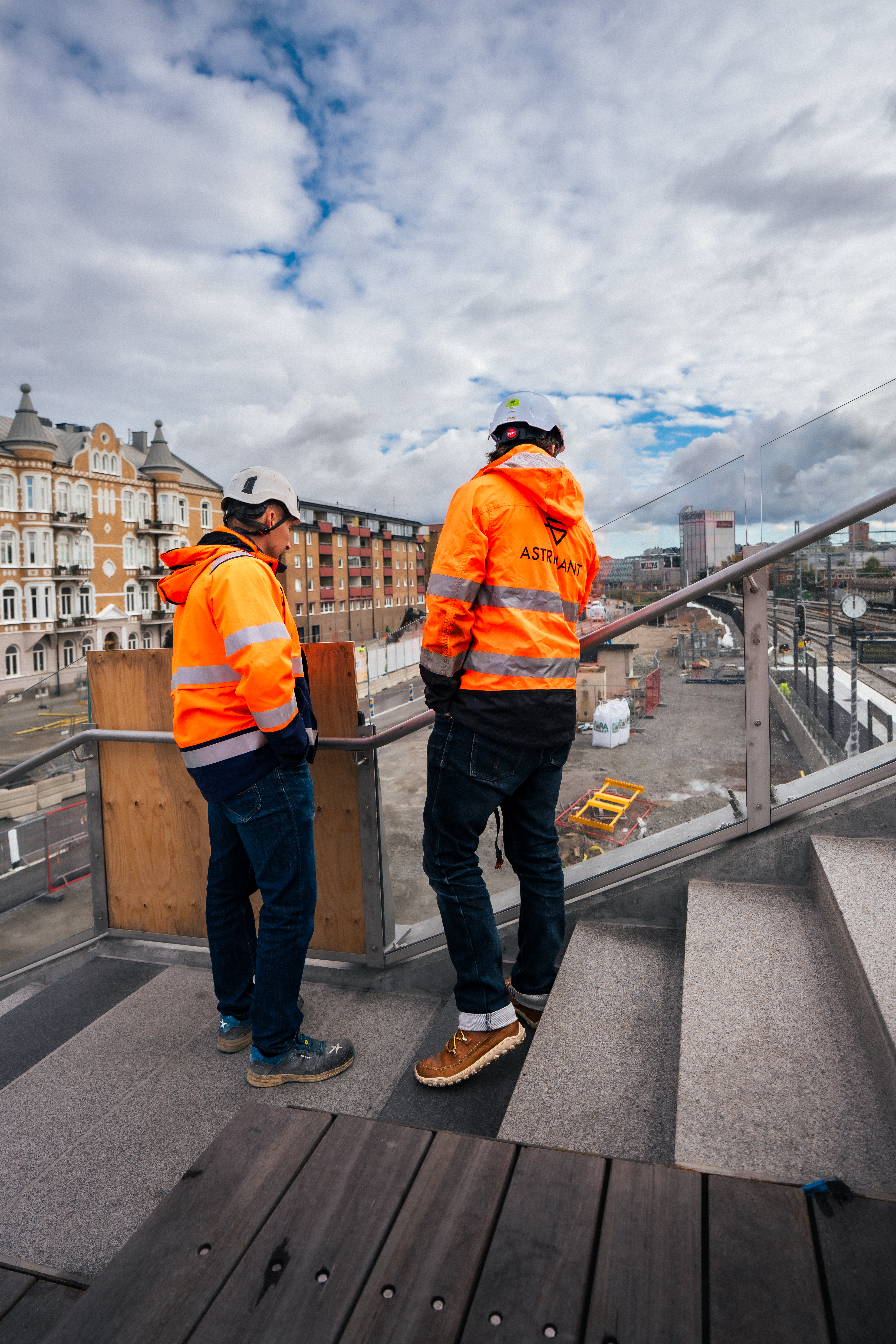 Två stenläggare från Astrimant tittar ner på resecentrum från trappan med granitbeklädnad i Karlstad